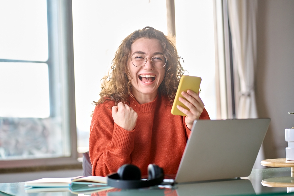 Young student receiving great news on smartphone in office