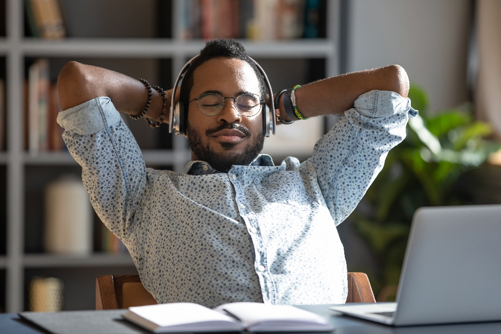 man wears headphones listening to music in office with computer open