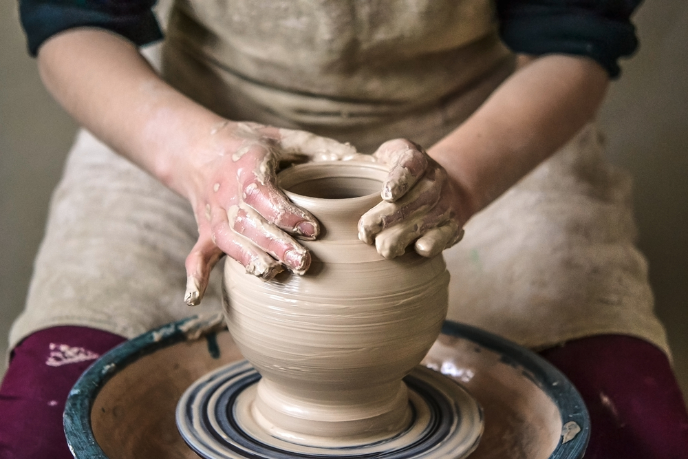 persons hands making a vase out of clay on a potters wheel