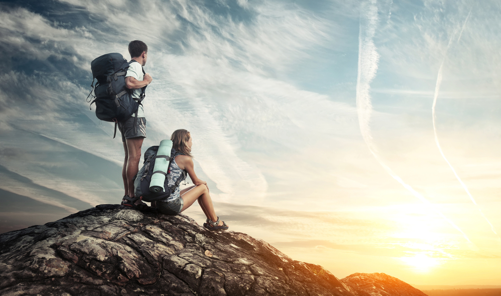 man and woman with hiking gear at top of cliff looking at the sunrise