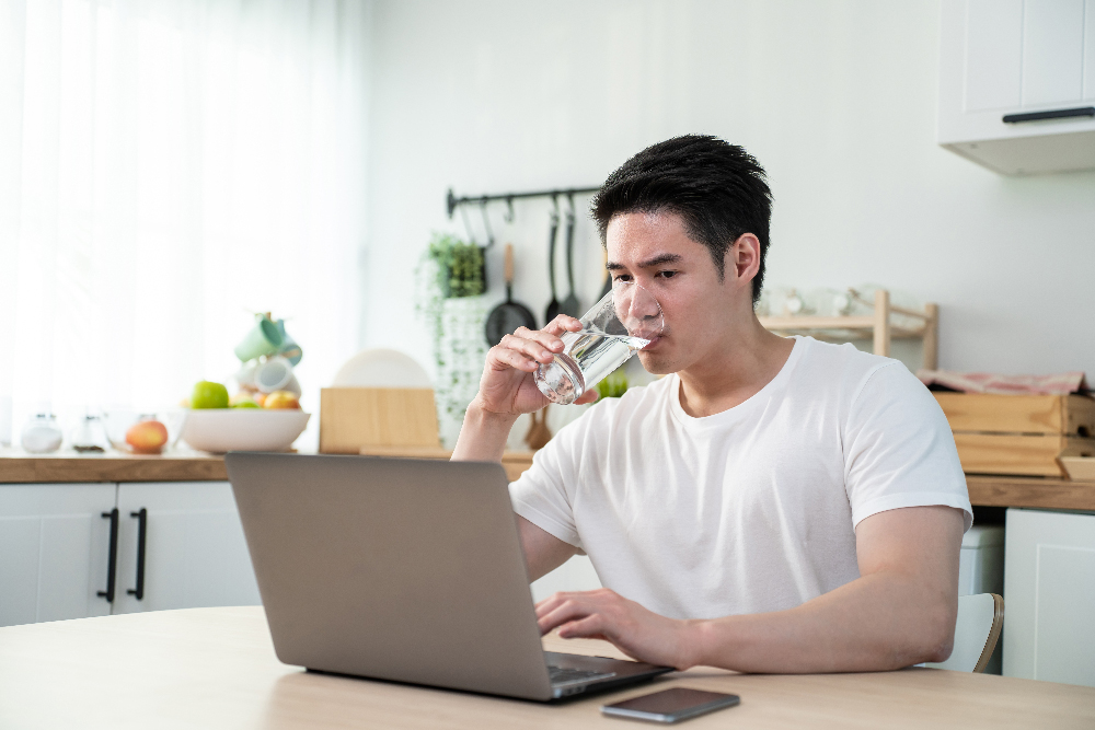 Man at desk with computer drinking glass of water