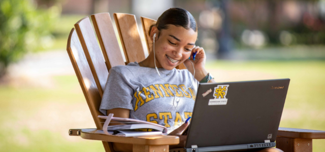 A student wearing a KSU shirt participating in a fun activity on her laptop